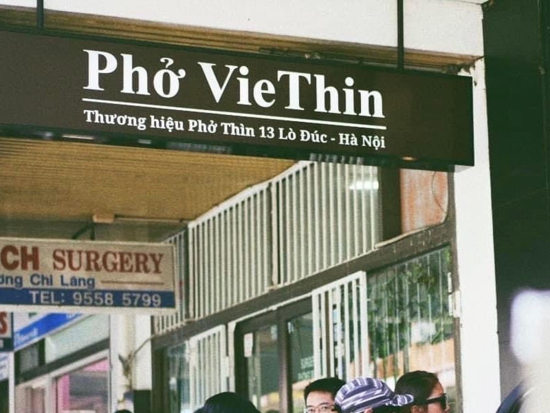 Biển hiệu quán ăn ghi 'Phở VieThin – Thương hiệu Phở Thìn 13 Lò Đức – Hà Nội' được treo trước cửa hàng. Phía dưới có nhiều người đứng xếp hàng, tạo cảm giác đông đúc và nổi tiếng.