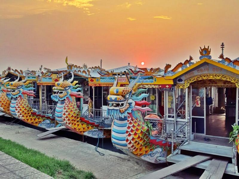 Dãy thuyền rồng sặc sỡ neo đậu tại bến Tòa Khâm ở Huế, dưới ánh hoàng hôn rực rỡ.