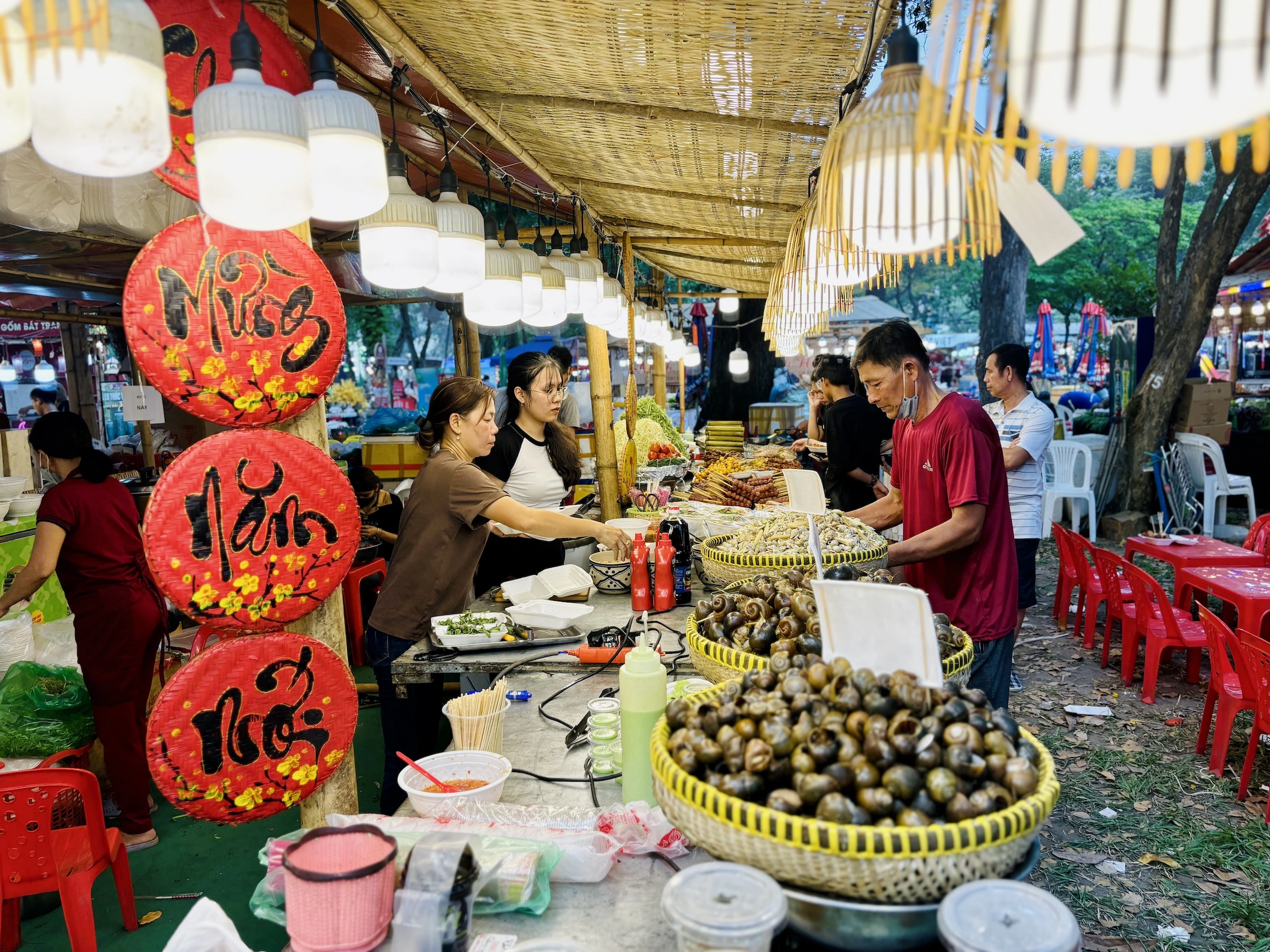 Gian hàng ẩm thực truyền thống với các món ăn dân dã như ốc luộc, xiên nướng trong lễ hội Tết Việt, trang trí bằng nón lá viết chữ thư pháp đỏ